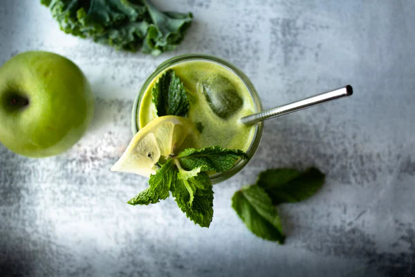 healthy green drink with a stainless straw and a green apple besides it